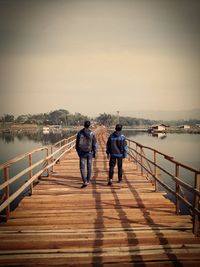 Rear view of people on pier over lake against sky