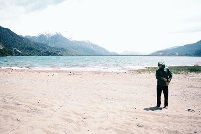 Rear view of man standing at beach against sky