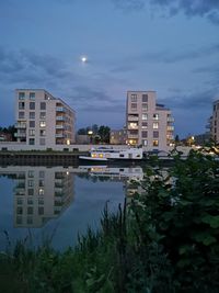 Buildings by river against sky in city at dusk