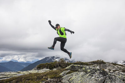 Trail runner jumps off rocks on mountain ridge.