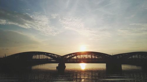Silhouette bridge over river against sky during sunset
