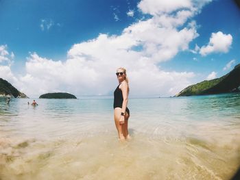 Side view of seductive woman standing on shore at beach against sky