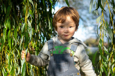 Portrait of cute boy standing outdoors under a willow tree 