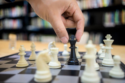 Cropped hand of man playing chess on table in library