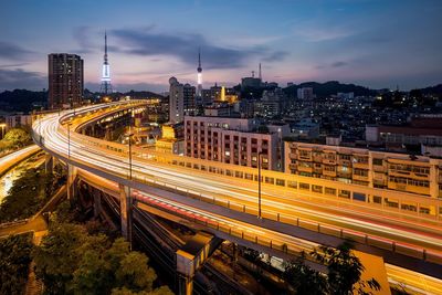 High angle view of light trails on road amidst buildings against sky