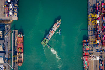 Aerial top view tugboat pushing container ship to quayside for load/unload container via crane 