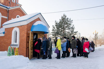 People on snow covered field against buildings