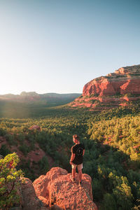 Rear view of man standing on mountain against clear sky