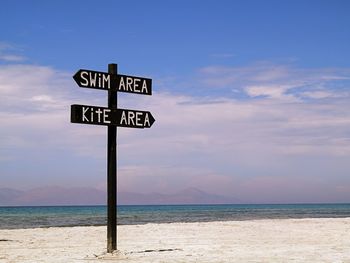 Information sign by sea against sky