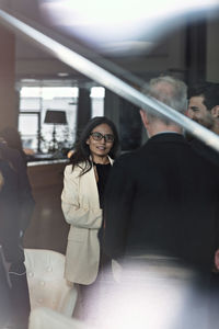 Businesswoman talking to male colleague while standing in lobby at office seen through window