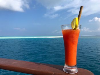 Glass of drink on sea against sky