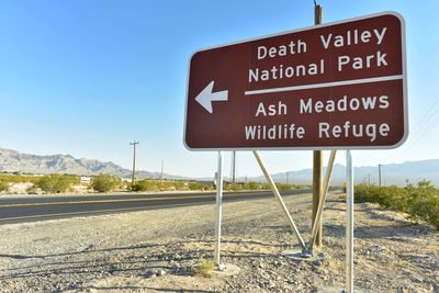 Death valley national park sign on field by road against clear blue sky
