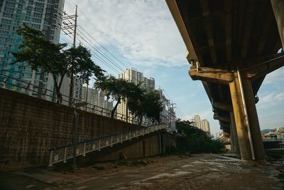 Low angle view of bridge by buildings against sky