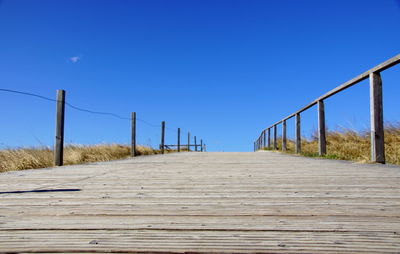 Surface level of boardwalk against clear blue sky