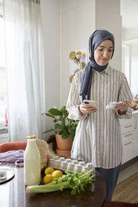 Woman in headscarf unpacking groceries at home and checking receipt