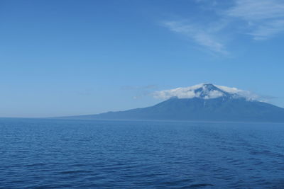 Scenic view of sea and snowcapped mountains against blue sky