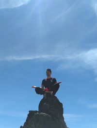 Low angle view of person standing on rock against sky