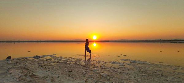 Woman standing on beach against sky during sunset