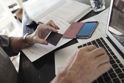 Cropped image of senior man holding credit card while using laptop at home