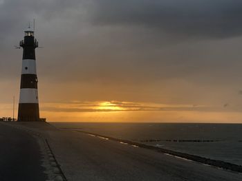 Lighthouse by sea against sky during sunset