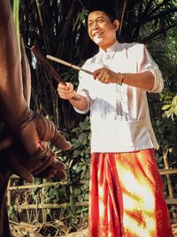 Happy young man holding sticks while standing by plants