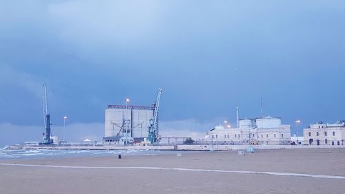 View of factory by sea against blue sky