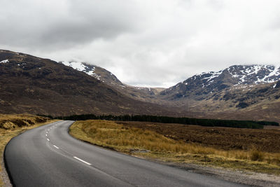 Country road by mountains against sky