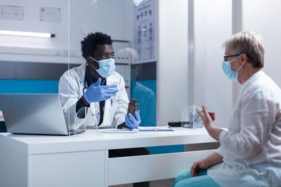 Doctor explaining medicine to patient through acrylic glass in clinic