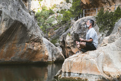 Man sitting on rock by waterfall