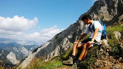 Teenage boy sitting on mountain against sky