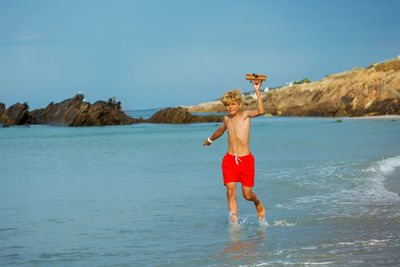 Full length of woman with arms outstretched standing at beach against sky