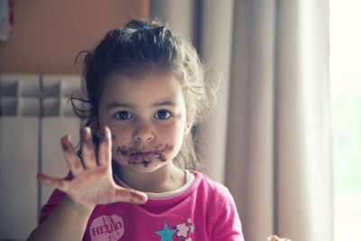 Portrait of cute girl gesturing with chocolate on her messy face while at home