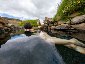 Rear view of woman lying down in water against sky