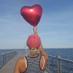 Rear view of woman with balloons against sea against sky