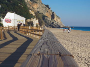 Railing on floorboard at beach against clear sky