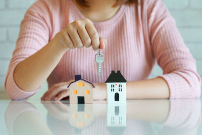 Midsection of woman holding key with model houses on table