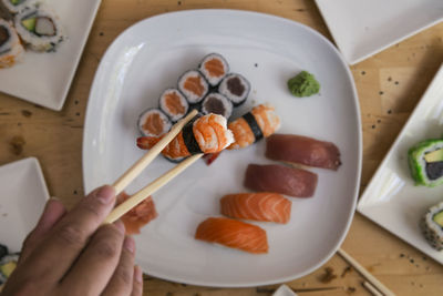 Cropped image of man holding sushi with chopsticks in plate, selective focus