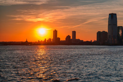 Sea by buildings against sky during sunset