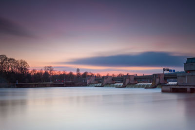 Scenic view of lake by buildings against sky during sunset