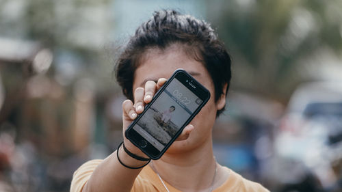 Close-up portrait of hand holding mobile phone outdoors