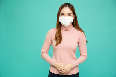 Portrait of young woman standing against blue background