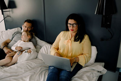 High angle view of woman using laptop while sitting by man and daughter on bed