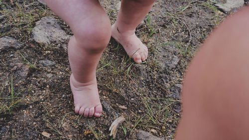 A small baby stands for the first time on dirt and gravel in the mountains on bare feet. 