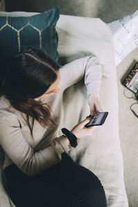 High angle view of teenage girl using mobile phone while lying on bed at home