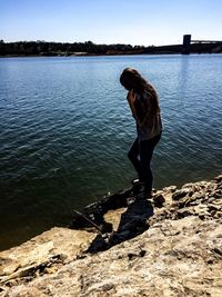 Full length side view of teenage girl standing on rock formation at riverbank