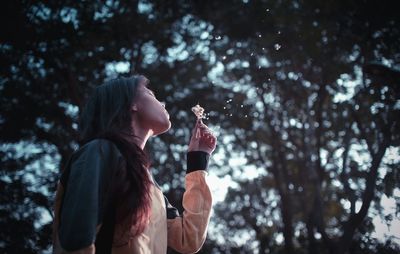 Low angle view of woman blowing flower seeds in forest