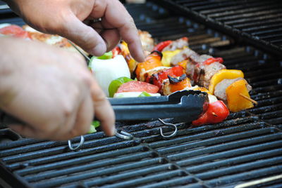 Cropped hand holding serving tongs by food in skewers on barbecue grill