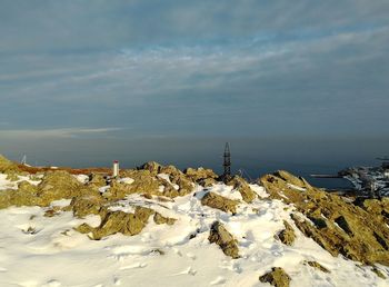 Snow covered rocks by sea against sky