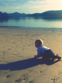 Boy sitting on beach against sky during sunset