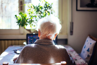 Rear view of senior woman using laptop while sitting at home